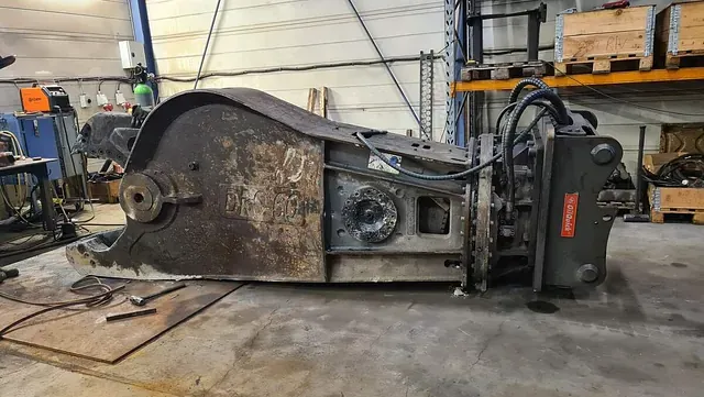 Slitt og rusten hydraulisk betongsaks ligger på verkstedgulv